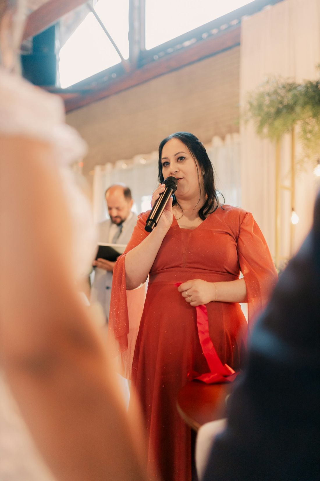 Bianca in a red dress speaking into a microphone at a wedding